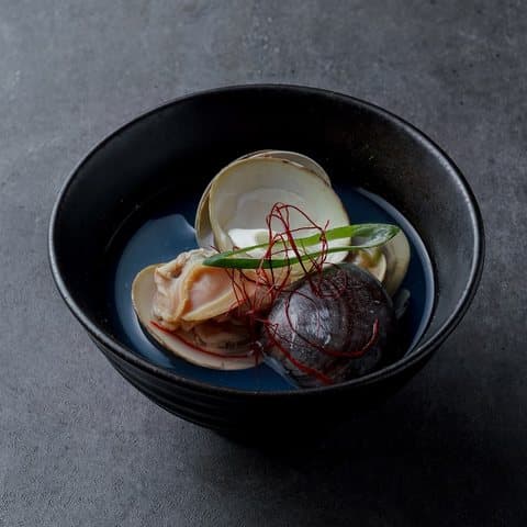 검은 그릇에 담긴 조개와 표고버섯 술찜