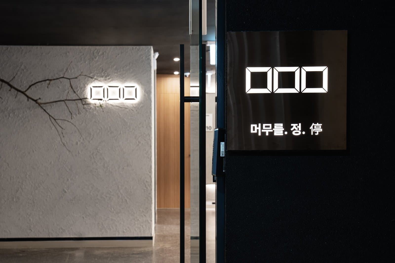 어두운 입구 벽에 불이 들어온 머무를정 로고 간판